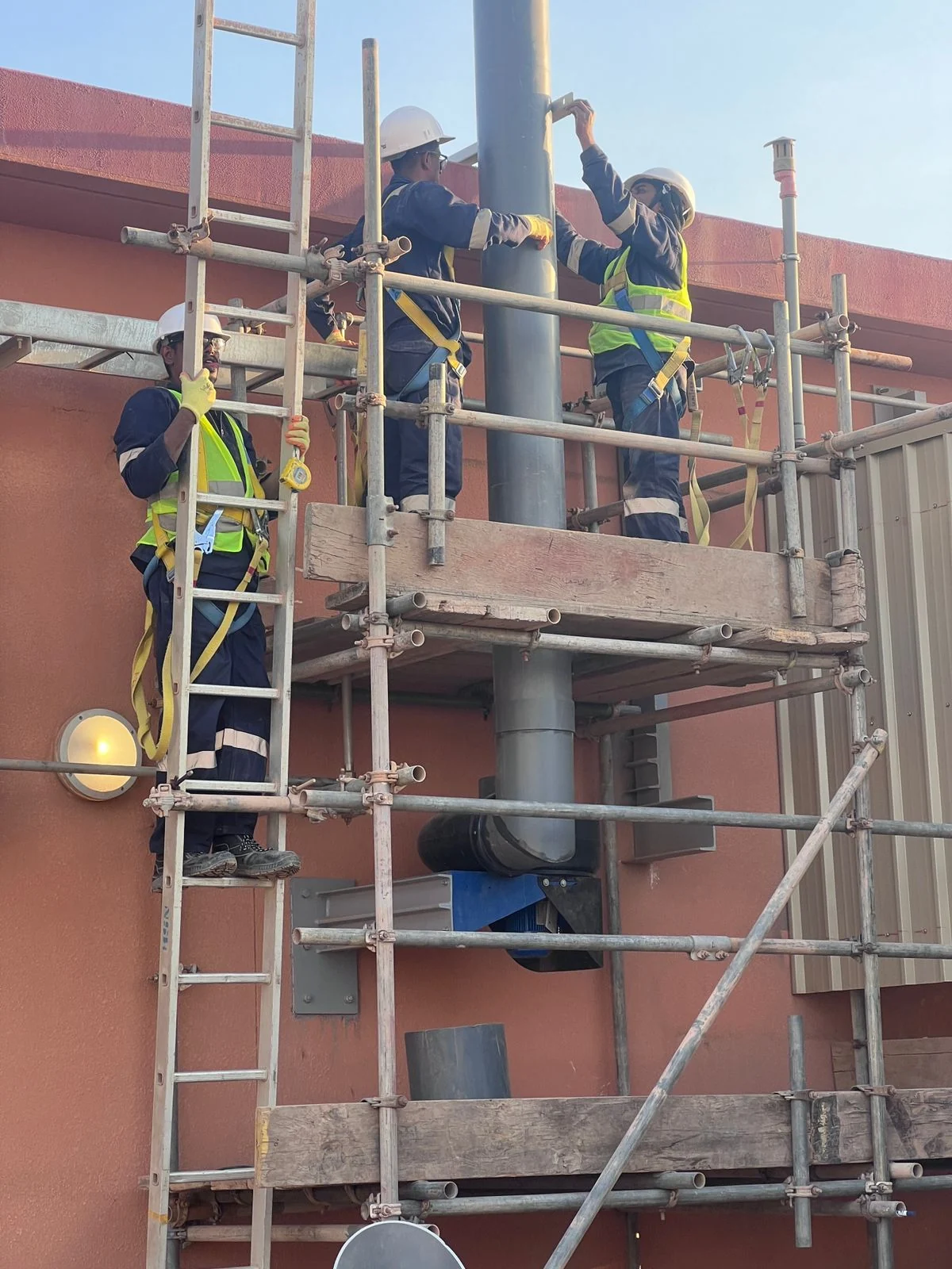 AAMCO technicians installing a vertical industrial ventilation stack from scaffolding